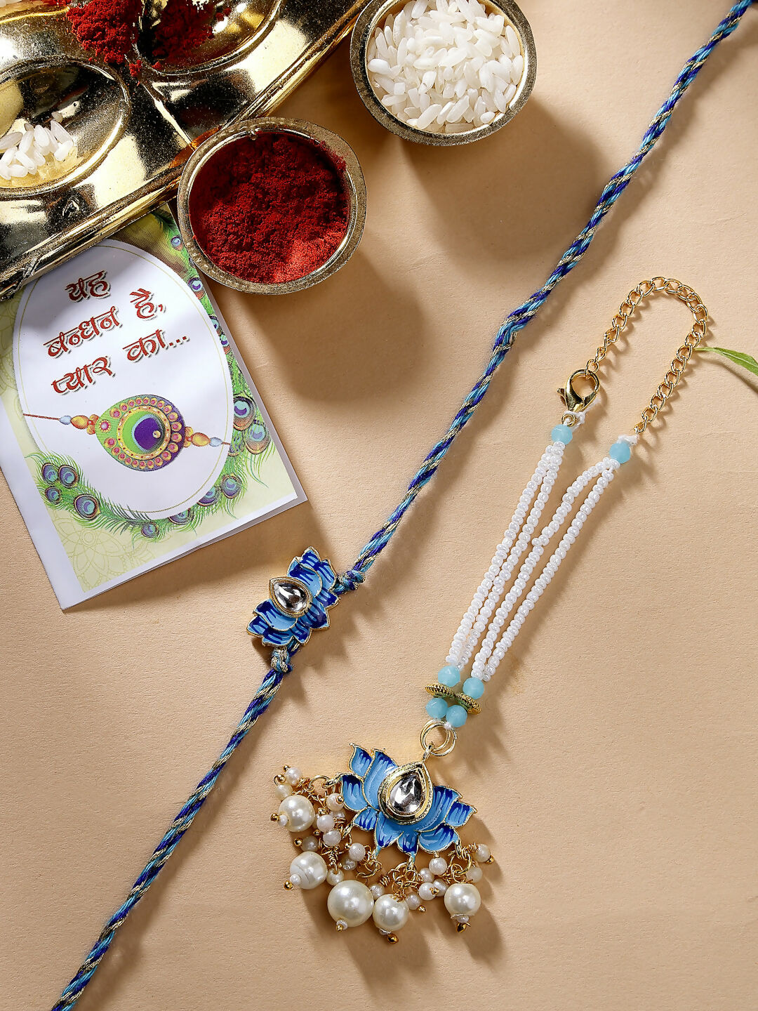 NVR Women & Men Set of 2 Blue Lotus Shape Kundan-Studded & Beaded Wraparound Rakhi Set With Roli Chawal & Chocolate